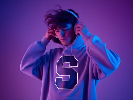 A young Caucasian male in a glowing hoodie listening to music with headphones under a purple light. photo
