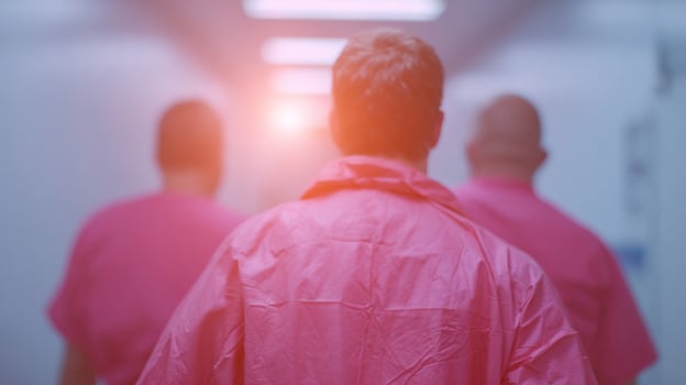 Men in gradient gowns stride through a sterile glow, echoing surreal hospital corridors, evoking Rare Disease Day photo