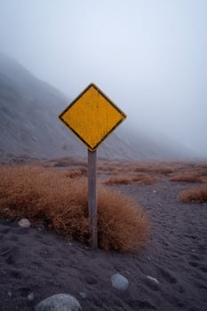 Misty desert crossroads, lone caution sign whispers autumn equinox riddles, Dia de los Muertos beckons, spectral hues blend photo
