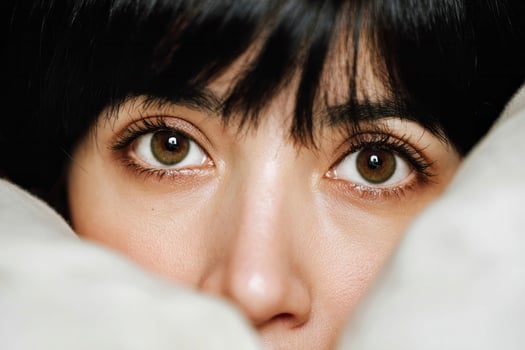 A contemplative Asian woman peers from beneath soft blankets, embodying coziness during Hygge season and Lunar New Year reflections photo