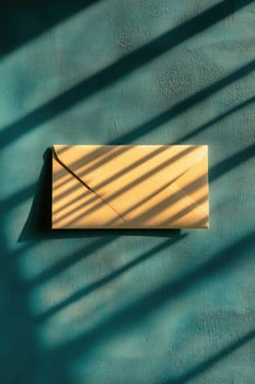Golden envelope rests on textured teal background beneath stark striped light shadows photo