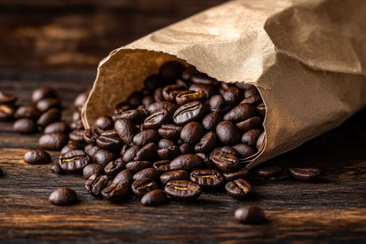 Roasted coffee beans spill from a brown kraft paper bag onto a wooden table photo