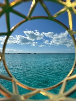 Serene turquoise ocean waters with scattered clouds under a sunny sky, viewed through a decorative golden circular frame in the Bahamas, showcasing tropical elegance and creative design, travel photo