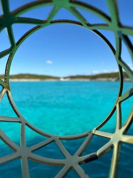Creative composition of turquoise ocean and distant shoreline viewed through an ornate circular metal framework under blue skies in the Bahamas, showcasing tropical beauty and artistic design, travel photo