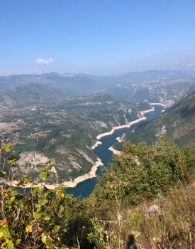 Aerial view of Lake Piva canyon in Montenegro surrounded by lush greenery and mountains under a clear blue sky, showcasing breathtaking natural beauty and serenity, concept of travel, nature photo