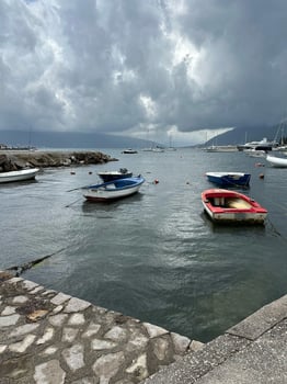 Small boats moored in a quiet harbor under dramatic storm clouds with distant hills and calm water, creating a serene atmosphere in Montenegro, showcasing natural beauty and tranquility travel photo
