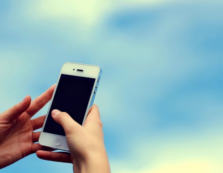 Person holding a white smartphone against a soft blue sky background photo