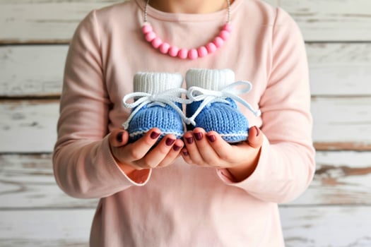Woman holding tiny blue knitted baby booties with white laces and trim photo