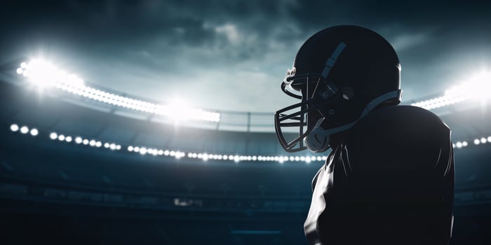 A silhouetted male football player stands ready on the field under bright stadium lights. photo