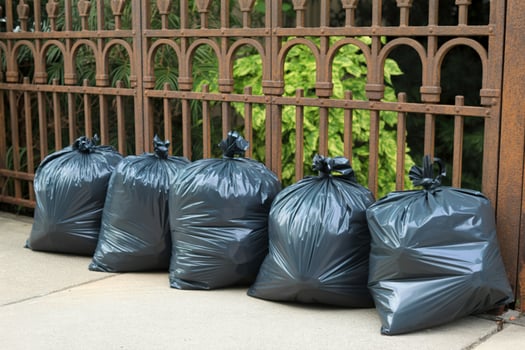Several full black garbage bags lined up against a rusty metal fence photo