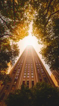 Towering beige skyscraper rises amidst trees, capturing architectural perspective from below in golden hour photo