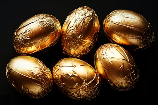 Six golden foil wrapped chocolate eggs arranged on a dark background photo