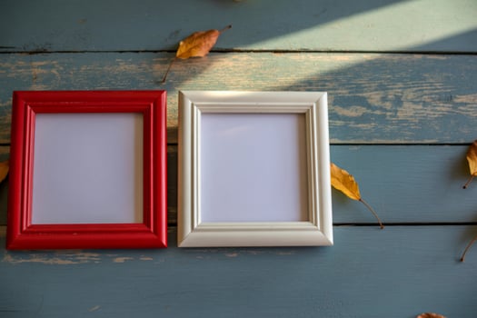 Two empty photo frames on a rustic wooden surface with autumn leaves