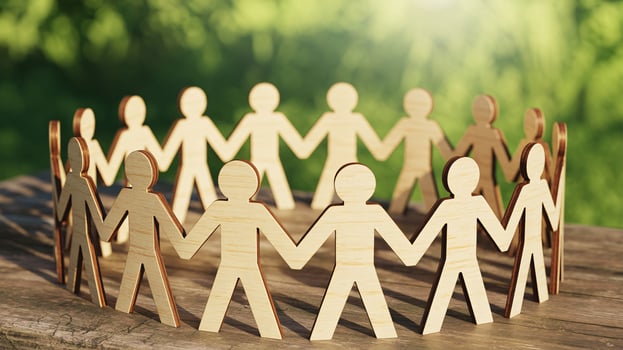 Wooden figures holding hands in a circle symbolize unity and collaboration in a green outdoor setting. photo
