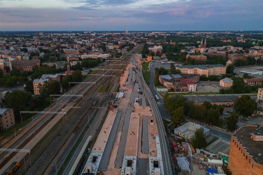 Aerial view of a construction site in Riga, Latvia, with train tracks, urban buildings, greenery, and landmarks like church spires and the Riga TV tower. photo