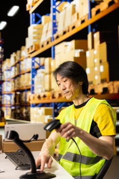 Asian worker in warehouse fulfillment center scanning packages and manages shipping labels with a barcode scanner, inventory control and data entry. Inventory tracking for e-commerce. photo