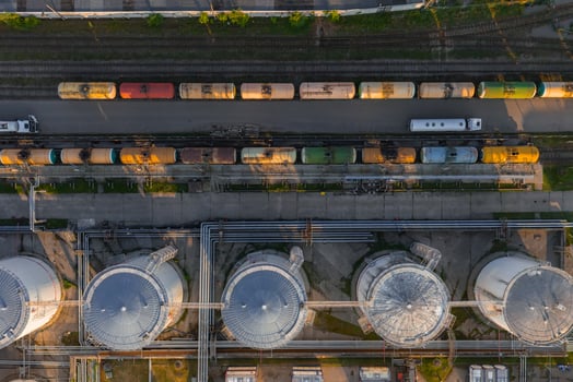 Aerial view of cylindrical storage tanks, freight train cars on tracks, and a truck in an industrial area in Riga, Latvia, under warm sunlight. photo