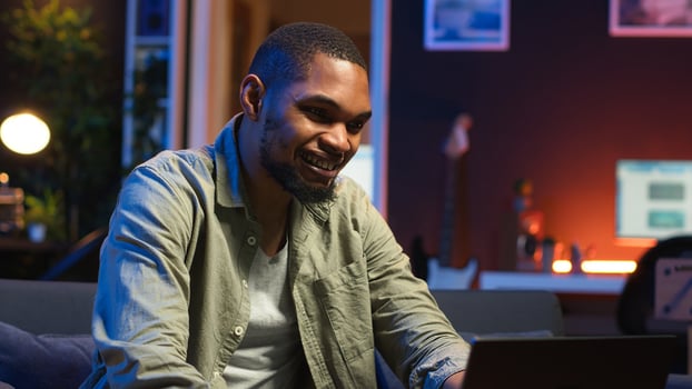 African american person being happy and proud with his project achievement, accomplishing multiple freelancing tasks at home. Young adult in the living room cheering. Camera B. photo
