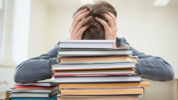 Stressed student overwhelmed by books, sitting at desk with hands on head. scene captures pressure of academic life and struggle to manage studies photo