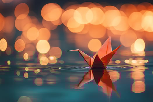 Orange paper crane rests gently on water surface reflecting bokeh lights beautifully photo