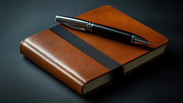 Shiny black pen rests on the brown leather journal with a black elastic band photo