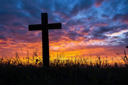 Wooden cross silhouette stands prominently against a vivid sunrise sky over a field photo