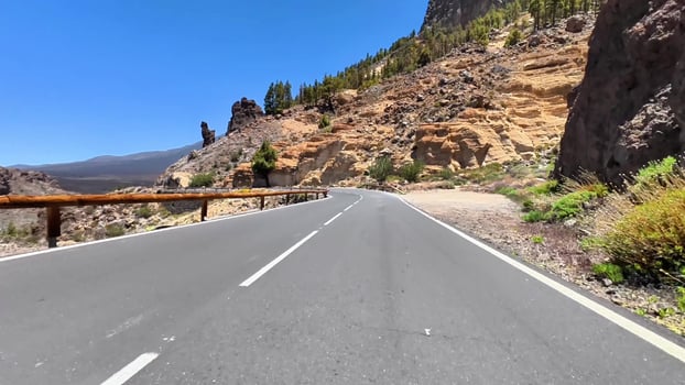 A stunningly beautiful road gracefully winds through rocky cliffs and vibrant lush greenery beneath a clear blue sky photo