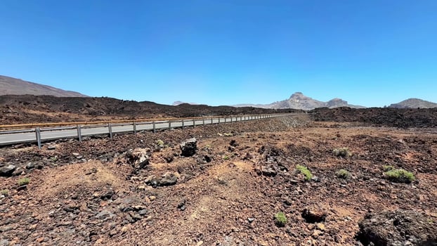 A stunning view of dramatic volcanic terrain with a winding road, rocky ground, and an expansive sky above photo