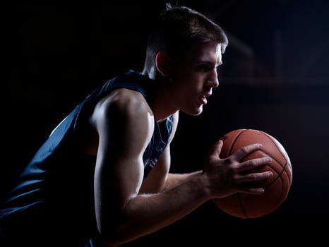 Male athlete focusing intensely while holding a basketball in a low-light setting. photo