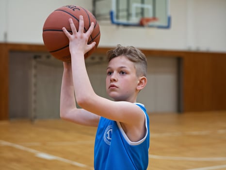 Young boy practicing basketball shot in a gym, focused expression and determined posture. photo