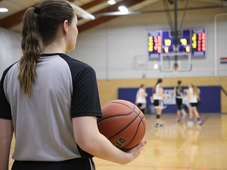 Female athlete in sports attire holding a basketball, watching teammates practice on the court. photo