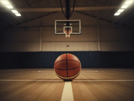 A basketball rests in the center of an indoor court, highlighting the hoop and wooden flooring. photo