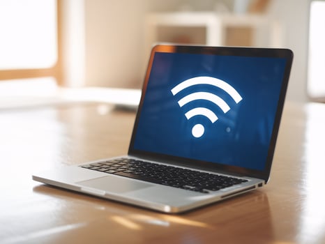 A laptop displaying a WiFi symbol on the screen, placed on a wooden table in a well-lit room. photo