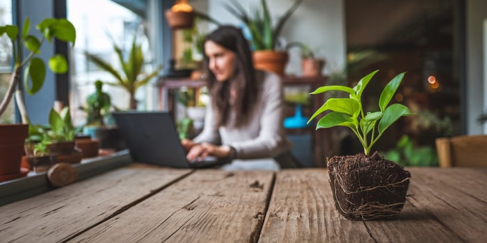Young woman working on her laptop in a cozy indoor garden, with a budding plant in focus. photo