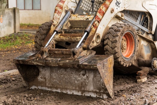 Close view shows a compact, dirty skid steer loader with a front-end bucket photo