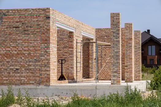 A brick house under construction has doorways and supporting pillars. Scaffolding and a hand truck are present photo