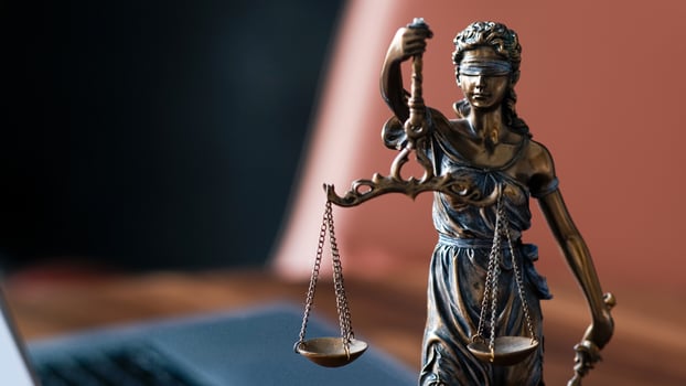 Bronze statue of Lady Justice holding scales, symbolizing fairness and law, positioned on a wooden desk with a laptop in the background, representing the legal profession and justice system photo