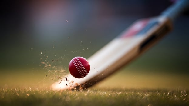 A red cricket ball collides with a bat, sending shards of grass flying in a dynamic sporting moment. photo
