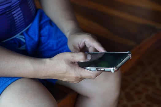 Close up man hands holding a smartphone, dressed in casual blue shorts. The image represents modern communication, internet connectivity, and accessing information or entertainment in daily life. photo