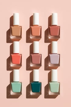 Nine square nail polish bottles with white caps arranged in a grid on pastel peach. Mixed shades, hard light and long shadows. Clean, unbranded beauty scene. photo