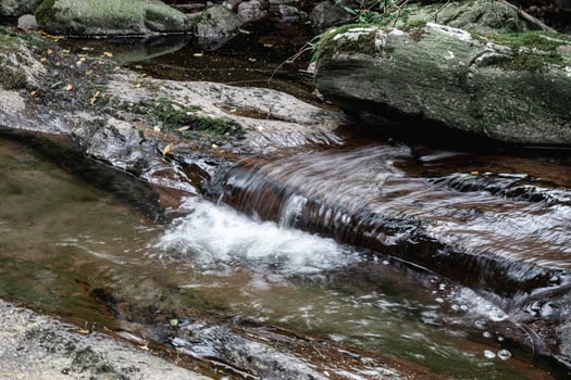 A Serene Stream is Flowing Gently Over the Rocky Terrain Surrounded by Natures Beauty photo