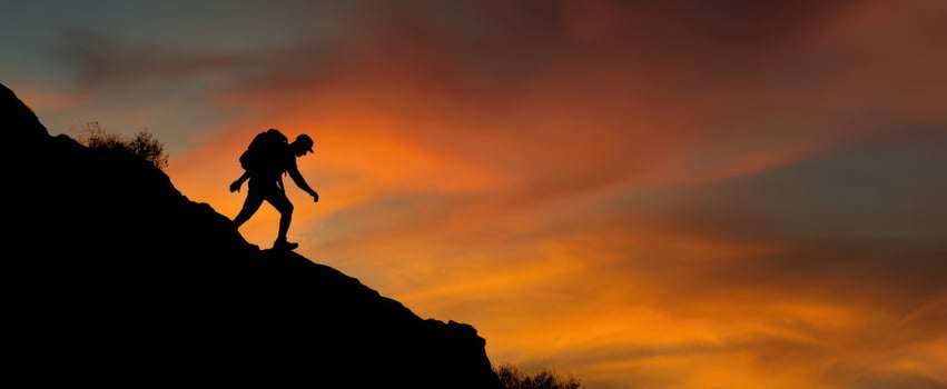 The silhouette of a hiker descending a rocky path at sunset. photo