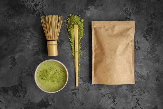 Matcha green tea with matcha latte or matcha latte in paper bag, whisk and cup of matcha latte on dark background, top view photo