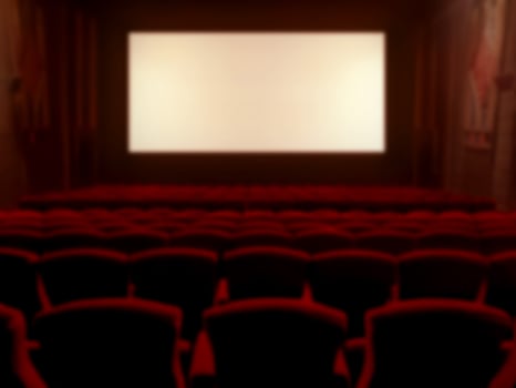 Blurred image of a classic movie theater with red velvet seats and a widescreen monitor. photo