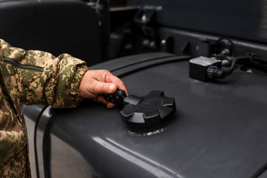 A hand in camouflage holds a gun filling the fuel tank of a military refueling vehicle photo