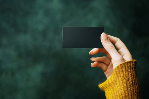 Hand Holding a Blank Black Business Card Over a Green Background in a Well-Lit Setting. photo