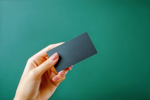 Hand Holding a Blank Black Business Card Over a Green Background in a Well-Lit Setting photo
