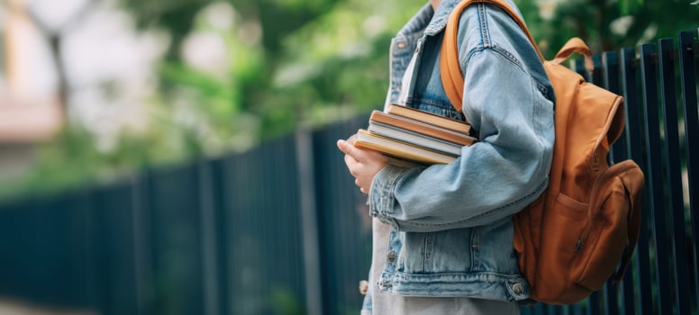 The Student Carrying Books and an Orange Backpack Along a Tree-Lined Campus Walkway photo
