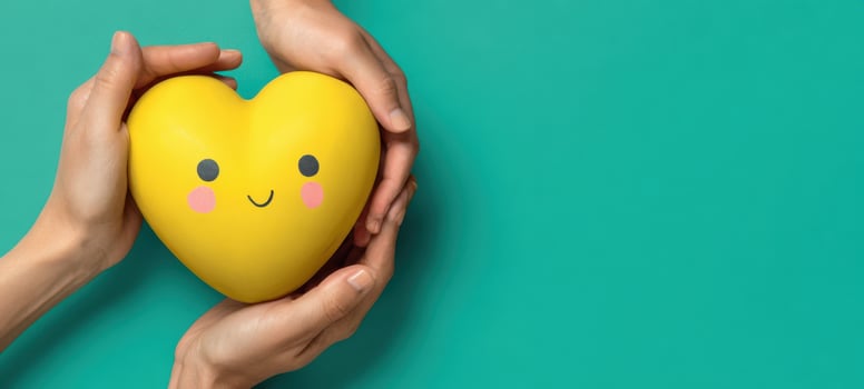 The Yellow Heart Toy Being Gently Held in Caring Hands on Teal Background photo