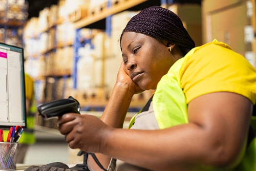 African american female napping on warehouse desk while she uses scanner, scanning shipping labels and barcode tags on a long shift. Tired overworked woman deals with burnout for e-commerce. photo